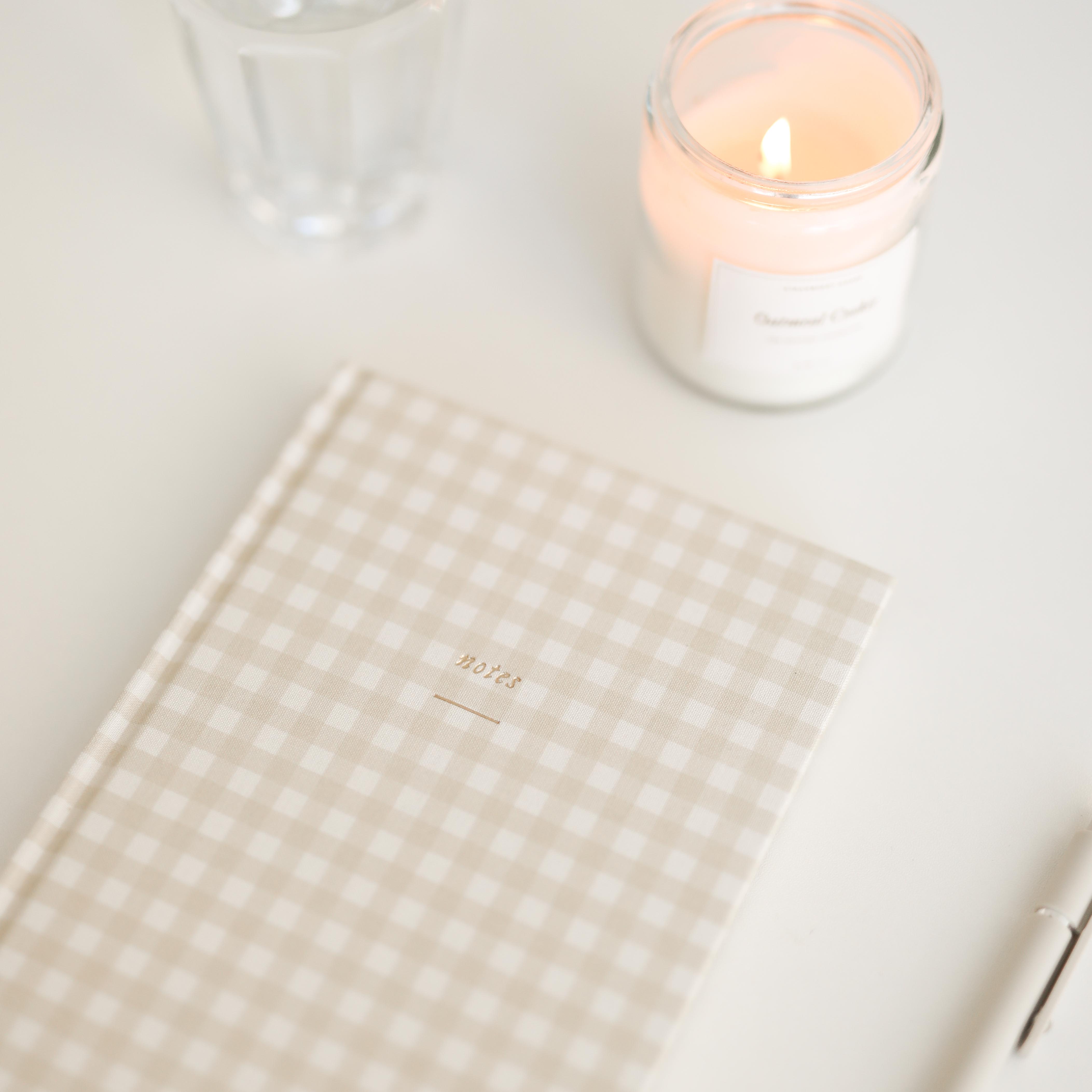 Gingham notebook and lit candle on a light surface