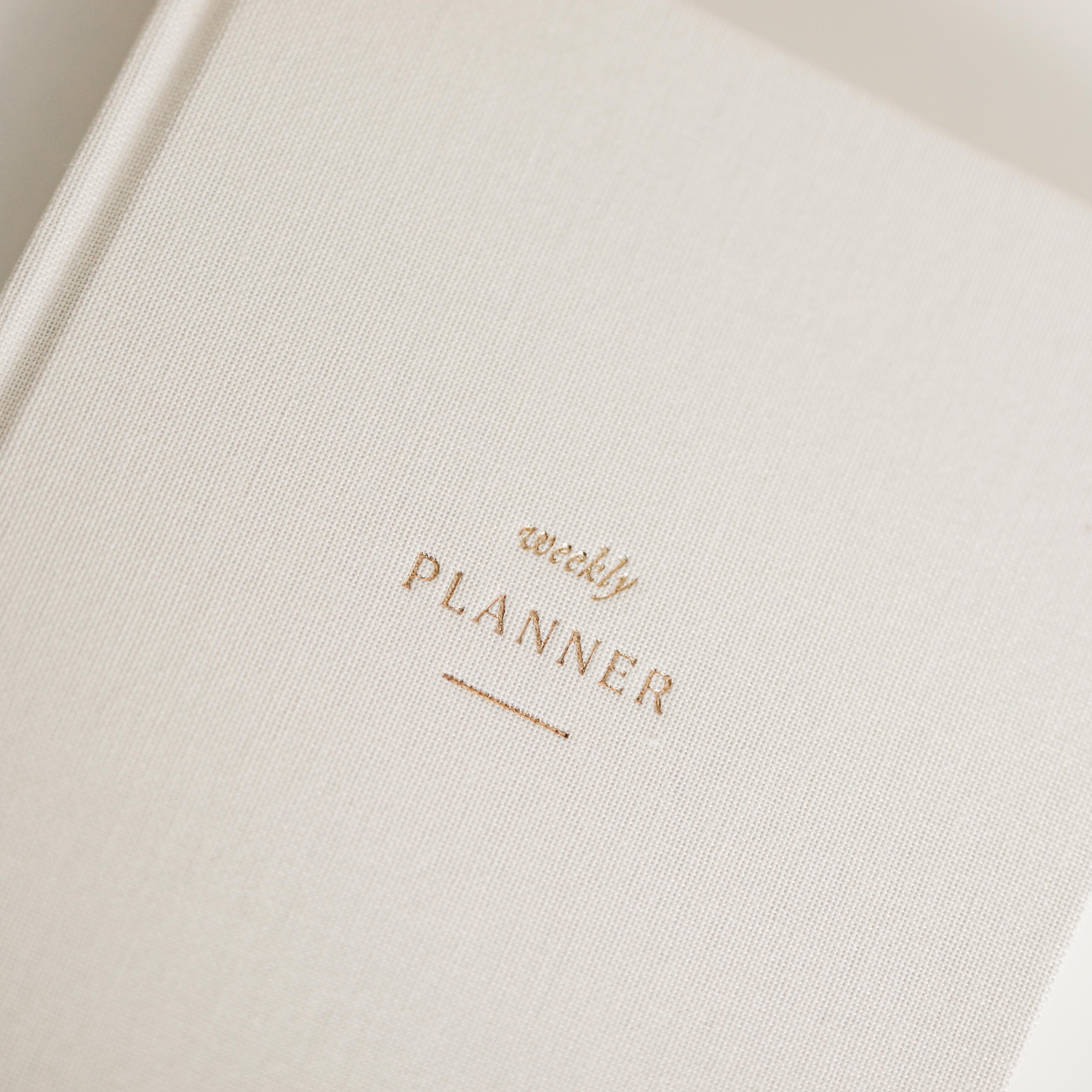 Close-up of a beige linen planner with 'weekly planner' text in gold foil