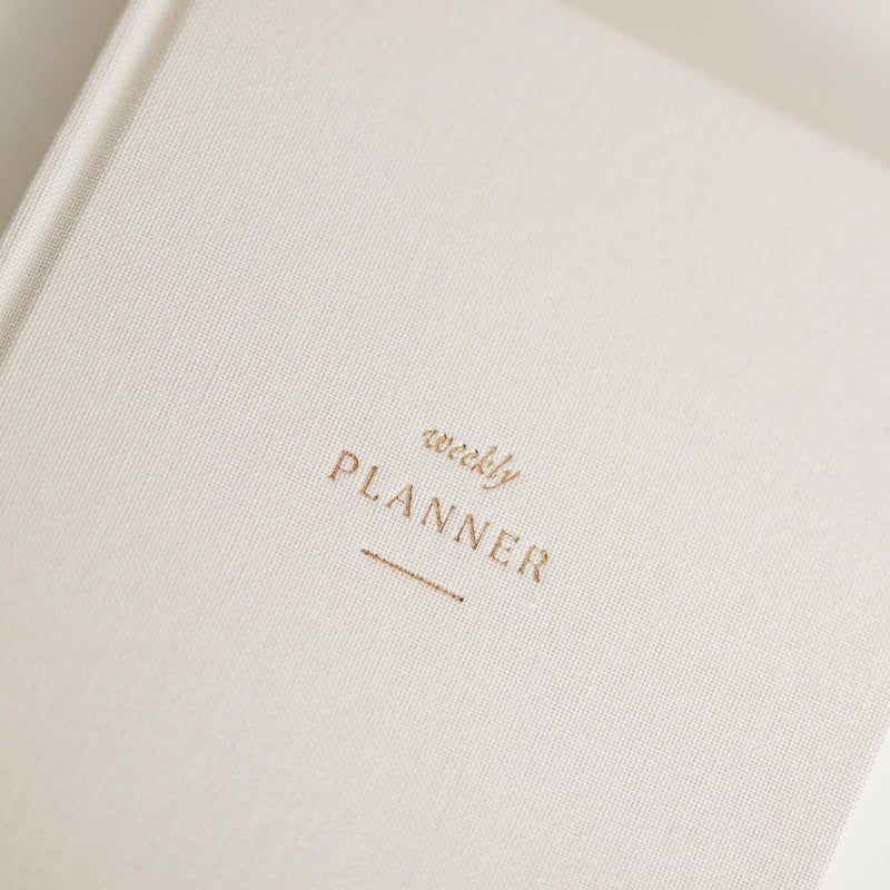 Close-up of a beige linen planner with 'weekly planner' text in gold foil